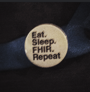 Close-up of a circular badge that says “Eat. Sleep. FHIR. Repeat.”, referencing HL7 FHIR in healthcare IT