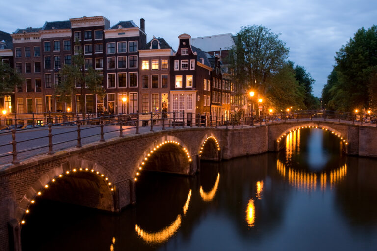Lit-up bridges and historic canal houses reflected in the water at night in Amsterdam